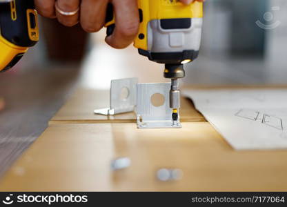 Man assembling furniture at home using a cordless screwdriver.. Man assembling furniture at home using a cordless screwdriver