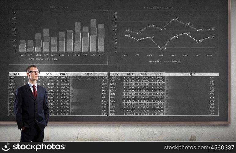 Man at blackboard. Young confident man wearing glasses standing near blackboard