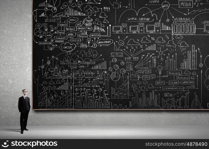 Man at blackboard. Young confident man wearing glasses standing near blackboard