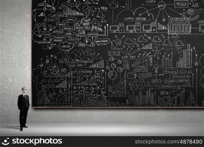 Man at blackboard. Young confident man wearing glasses standing near blackboard