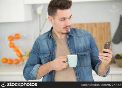 man at home holding cup and looking at smartphone