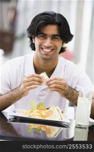 Man at restaurant eating sandwich and smiling (selective focus)