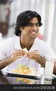 Man at restaurant eating sandwich and smiling (selective focus)