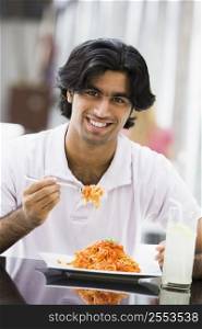 Man at restaurant eating spaghetti and smiling (selective focus)
