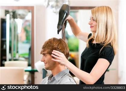 Man at the hairdresser, she has finished the cut and is drying his hair with a blow dryer