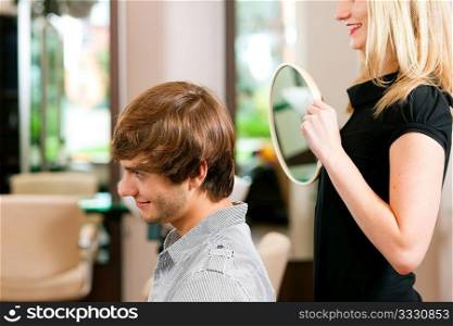 Man at the hairdresser, she has finished the cut and is showing the result in the mirror