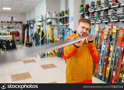 Man at the showcase checks the surface of the ski, shopping in sports shop. Winter season extreme lifestyle, active leisure store, customer buying skiing equipment