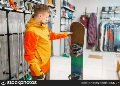 Man at the showcase choosing snowboard, shopping in sports shop. Winter season extreme lifestyle, active leisure store, customer buying skiing equipment. Man choosing snowboard, shopping in sports shop