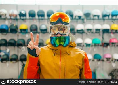 Man at the showcase trying on three masks for ski or snowboarding, front view, shopping in sports shop. Winter season extreme lifestyle, active leisure store, buyers choosing protect equipment. Man trying on three masks for ski or snowboarding