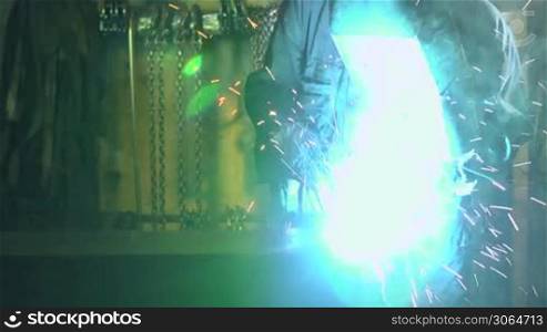 Man at work in industrial facility using welding mask, tools and equipment on metal