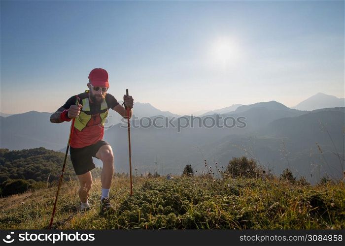 Man athlete of sky-raid in the mountains with poles sticks uphill.