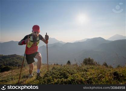 Man athlete of sky-raid in the mountains with poles sticks uphill.