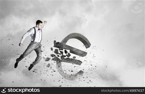 Man attacking euro symbol. Determined businessman in anger breaking stone euro sign