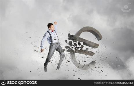Man attacking euro symbol. Determined businessman in anger breaking stone euro sign