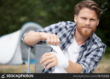 man bandaging arm during camping holiday