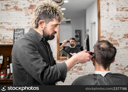 Man barber cutting hair of male client with clipper at barber shop. Hairstyling process. High quality photography. Man barber cutting hair of male client with clipper at barber shop. Hairstyling process.