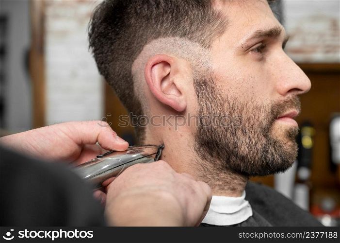 Man barber cutting hair of male client with clipper at barber shop. Hairstyling process. High quality photography. Man barber cutting hair of male client with clipper at barber shop. Hairstyling process.