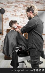 Man barber cutting hair of male client with clipper at barber shop. Hairstyling process. High quality photography. Man barber cutting hair of male client with clipper at barber shop. Hairstyling process.