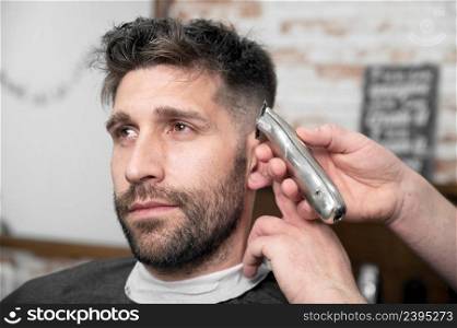 Man barber cutting hair of male client with clipper at barber shop. Hairstyling process. High quality photography. Man barber cutting hair of male client with clipper at barber shop. Hairstyling process. 