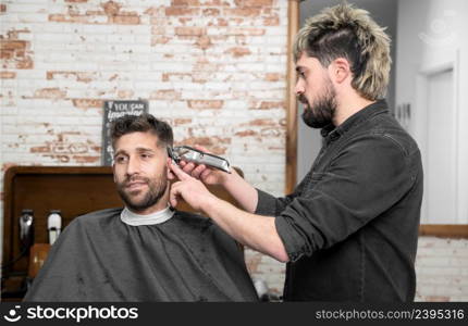 Man barber cutting hair of male client with clipper at barber shop. Hairstyling process. High quality photography. Man barber cutting hair of male client with clipper at barber shop. Hairstyling process.