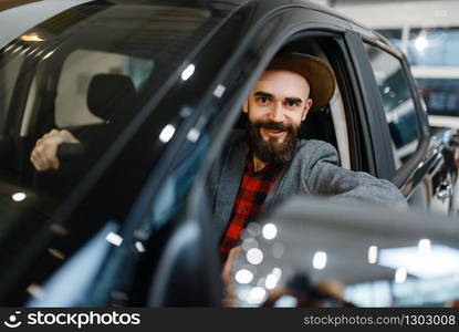 Man behind the wheel of pickup truck in car dealership. Customer in vehicle showroom, male person buying transport, auto dealer business. Man behind the wheel of truck in car dealership