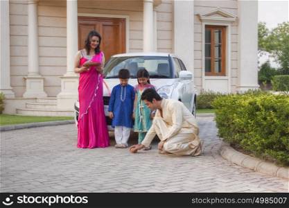 Man breaking coconut on ground as family watches on