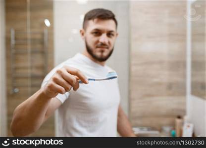 Man brushes his teeth in bathroom, front view on face, routine morning hygiene. Male person at the sink performs skin and body treatment procedures. Man brushes his teeth in bathroom, morning hygiene