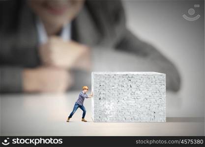 Man builder. Businesswoman looking at miniature of builder pushing wall