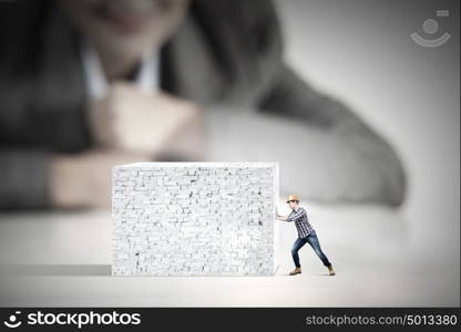 Man builder. Businesswoman looking at miniature of builder pushing wall