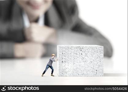 Man builder. Businesswoman looking at miniature of builder pushing wall
