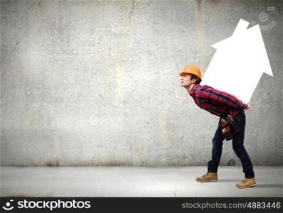 Man builder presenting something. Young smiling craftsman carrying house model on back