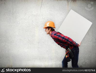 Man builder presenting something. Young smiling craftsman carrying white cube on back