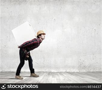 Man builder presenting something. Young smiling craftsman carrying white cube on back