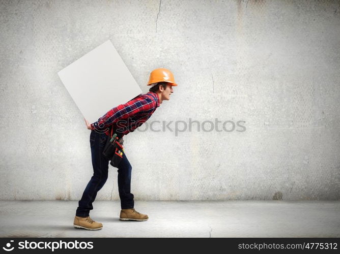 Man builder presenting something. Young smiling craftsman carrying white cube on back