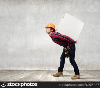 Man builder presenting something. Young smiling craftsman carrying white cube on back