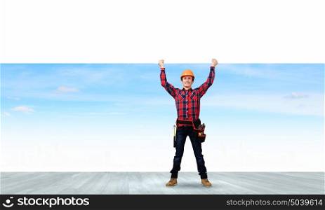 Man builder presenting something. Young smiling craftsman holding white blank banner above head