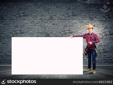 Man builder presenting something. Young smiling craftsman holding with blank banner. Place for text