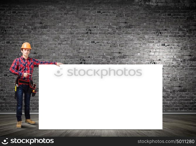 Man builder presenting something. Young smiling craftsman holding with blank banner. Place for text