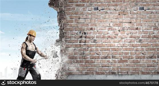 Man builder. Strong man in uniform breaking brick wall with hammer