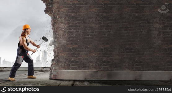 Man builder. Strong man in uniform breaking brick wall with hammer