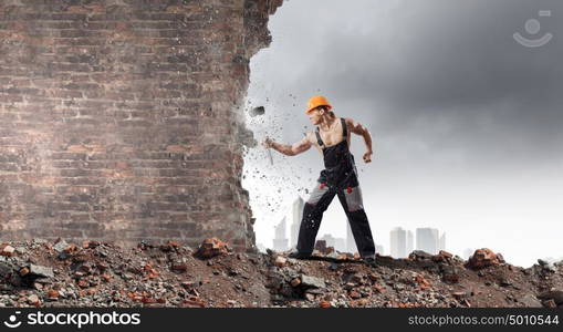 Man builder. Strong man in uniform breaking brick wall with hammer