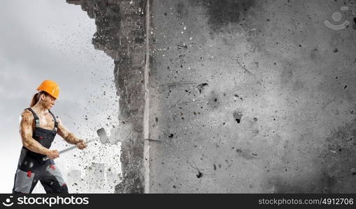 Man builder. Strong man in uniform breaking wall with hammer