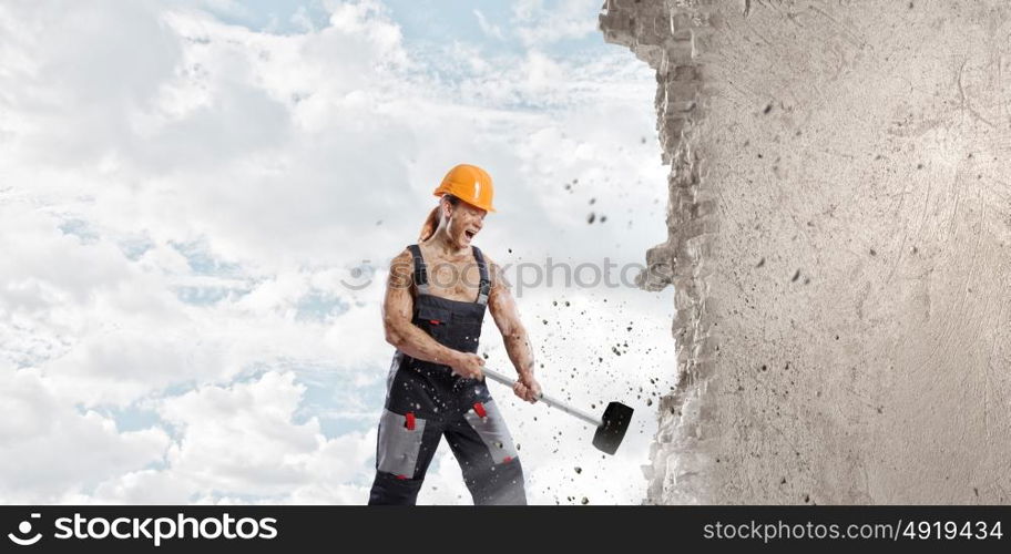 Man builder. Strong man in uniform breaking wall with hammer