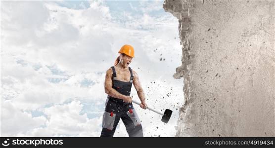 Man builder. Strong man in uniform breaking wall with hammer