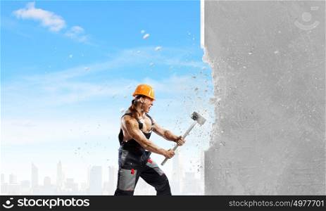 Man builder. Strong man in uniform breaking wall with hammer