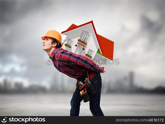 Man builder. Young smiling craftsman carrying house model on back