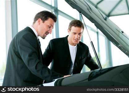 Man buying a car in dealership looking under the hood at the engine