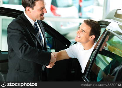 Man buying a car in dealership sitting in his new auto; they are shaking hands to close the deal