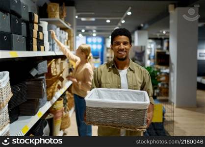 Man buying wicker basket in shop standing and looking at camera. Young couple shopping. Man buying wicker basket standing in shop