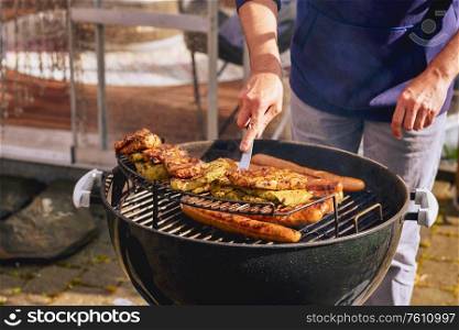 Man by the barbeque with pork chops and sausages on a hot summer day